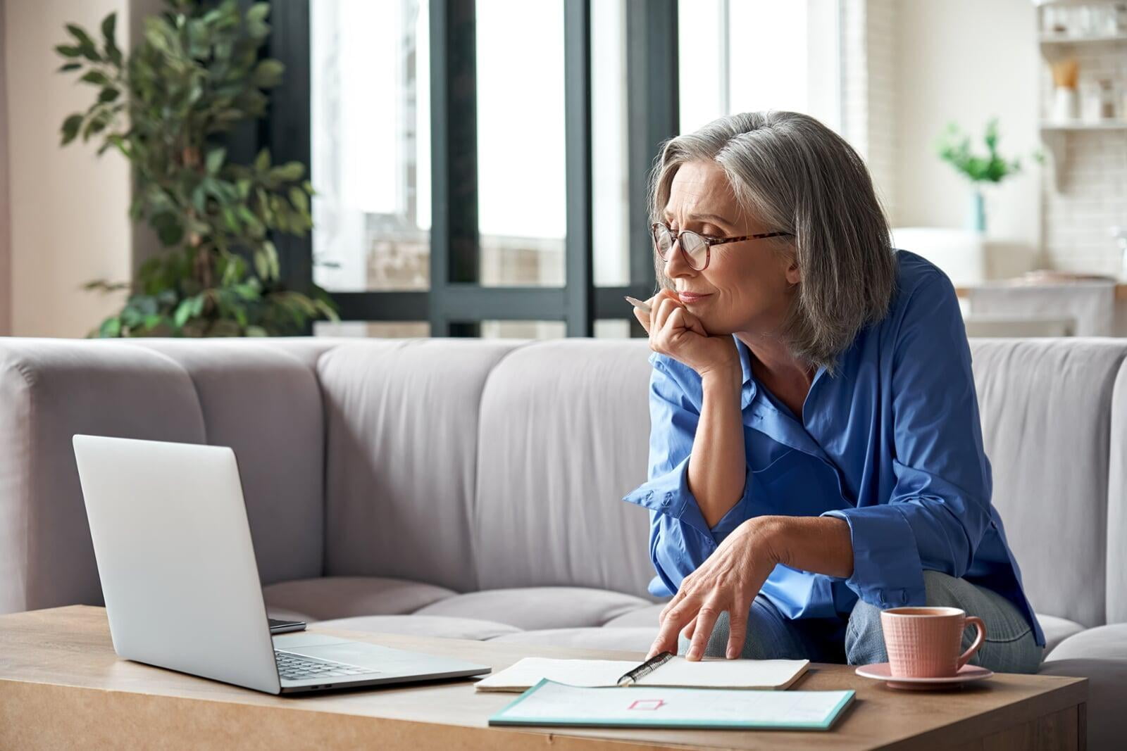 Adult aged user looking at laptop with notebooks on table. 